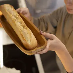 Frau hält Holzschale mit Baguette zum Auftauen.