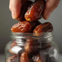 Eine Hand legt saftige Datteln in ein Glas. Perfekt zum Einfrieren und für süße Momente.
