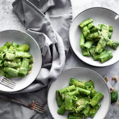 Drei Teller mit Rigatoni in cremiger, grüner veganer Spinatsoße, bestreut mit veganem Parmesan. Ein Genuss für Augen und Gaumen!