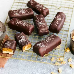 Vegane Snickers mit Karamell, Erdnüssen und Meersalz bestreut, auf einem goldenen Gitter.