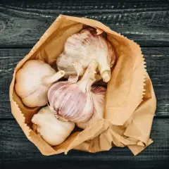 Frische Knoblauchzehen in einer Papiertüte, bereit zum **knoblauch lagern** auf dunklem Holz.