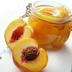 Saftige Pfirsiche in einem Glas, bereit zum Lagern. Daneben liegen frische, aufgeschnittene Früchte.