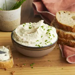 Cremiger veganer Frischkäse, garniert mit Schnittlauch, wird auf Brot gestrichen. Perfekt, um veganen Frischkäse selber machen zu lernen.