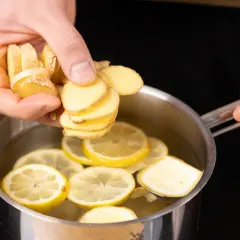Frische Ingwerscheiben werden in einen Topf mit heißem Wasser und Zitronenscheiben gegeben, um einen wärmenden Ingwer-Zitronen-Tee zuzubereiten.