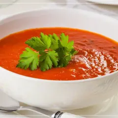 Eine Schüssel cremiger Tomatensuppe mit Petersilie garniert, daneben ein Löffel.