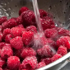 Frische Himbeeren werden in einem Sieb unter fließendem Wasser gewaschen, um sie für die Lagerung vorzubereiten und **frisch zu halten**.