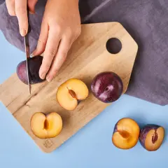 Hände schneiden Pflaumen auf einem Holzbrett. Die Früchte werden für die Lagerung vorbereitet.