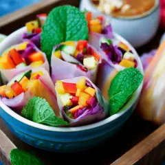Bunte low carb sommerrollen gefüllt mit Gemüse und Minze, serviert in einer blauen Schüssel auf einem Holzteller.