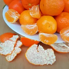Ein Teller voller saftiger Mandarinen, einige geschält und in Spalten geteilt, daneben die orangen Schalen. Perfekt zum Lagern und Genießen.