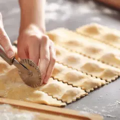 Hände schneiden mit einem Teigrädchen frisch gemachte Ravioli. So lassen sich selbstgemachte Ravioli aufbewahren.