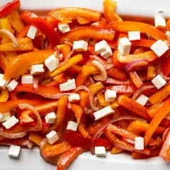 Bunter Paprika Salat mit Feta-Würfeln und roten Zwiebeln auf einem weißen Teller.