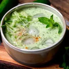 Erfrischende cremige kalte Gurkensuppe mit Eiswürfeln, Minze und geriebenen Gurken, garniert mit Pfeffer und Paprikapulver.