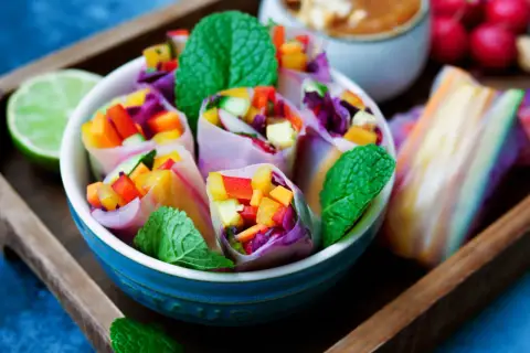 Bunte low carb sommerrollen gefüllt mit Gemüse und Minze, serviert in einer blauen Schüssel auf einem Holzteller.
