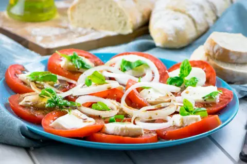 Tomaten-Mozzarella-Salat mit Zwiebelringen und Basilikum, beträufelt mit einem leckeren Dressing. Dazu frisches Brot.
