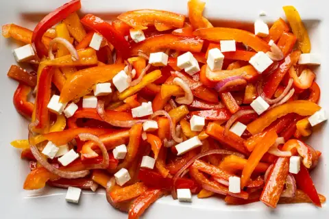Bunter Paprika Salat mit Feta-Würfeln und roten Zwiebeln auf einem weißen Teller.