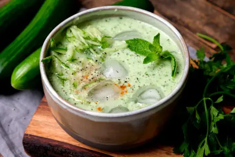 Erfrischende cremige kalte Gurkensuppe mit Eiswürfeln, Minze und geriebenen Gurken, garniert mit Pfeffer und Paprikapulver.