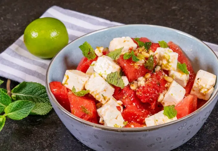 Erfrischender Wassermelone Feta Salat mit Minze und Pinienkernen, garniert mit Limettenabrieb. Ein leichter Genuss.