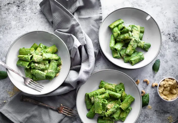 Drei Teller mit Rigatoni in cremiger, grüner veganer Spinatsoße, bestreut mit veganem Parmesan. Ein Genuss für Augen und Gaumen!