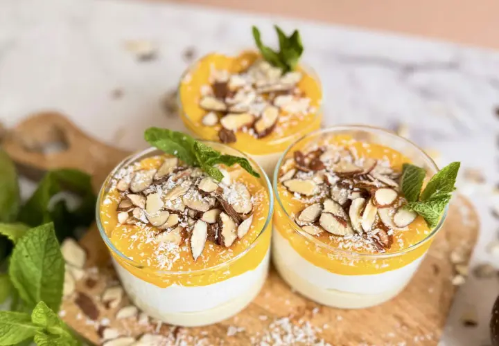 Drei Gläser mit cremigem Kokos Dessert vegan, garniert mit Mango-Püree, Mandelblättchen und Kokosraspeln.
