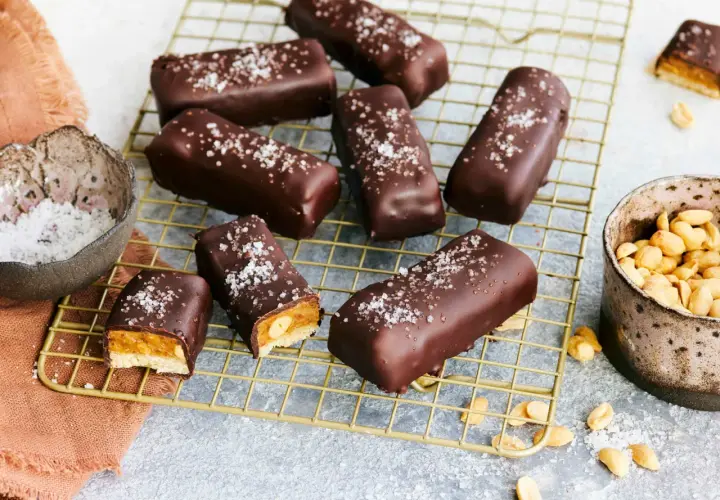 Vegane Snickers mit Karamell, Erdnüssen und Meersalz bestreut, auf einem goldenen Gitter.
