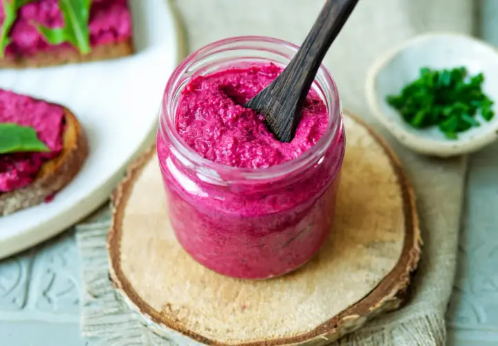Glas mit cremigem, veganem Rote Bete Aufstrich, daneben Brot mit Aufstrich und Schnittlauch.