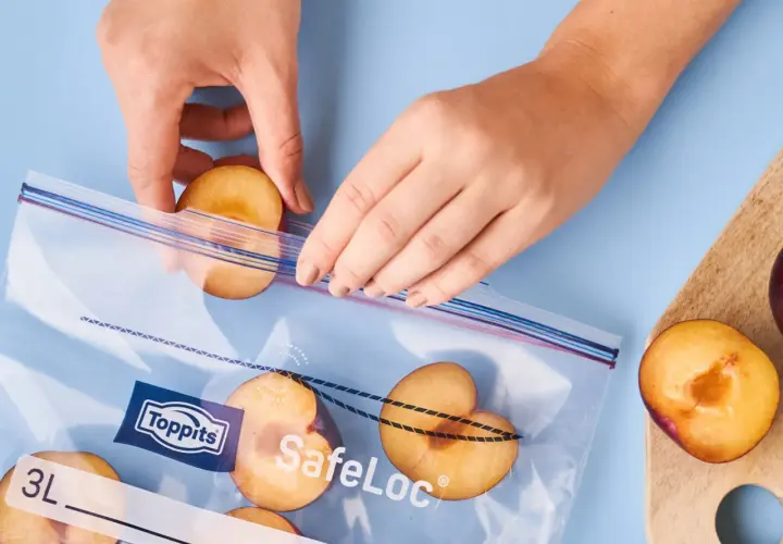 Hände legen Pflaumenhälften in einen Toppits SafeLoc Beutel zum Einfrieren. So bleiben die Früchte lange frisch.