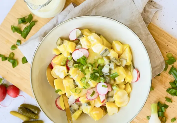 Ein cremiger veganer Kartoffelsalat mit Mayo, Radieschen und Gurken, garniert mit Frühlingszwiebeln.