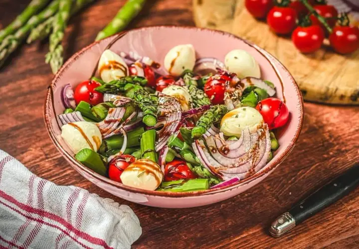 Frischer Spargelsalat mit Ei, Tomaten, roten Zwiebeln und Mozzarella-Kugeln, beträufelt mit Balsamico-Dressing.