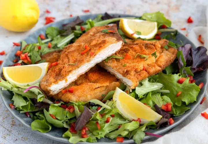 Knuspriges, low carb Putenschnitzel auf einem Salatbett mit Zitronenspalten und Paprikastückchen.