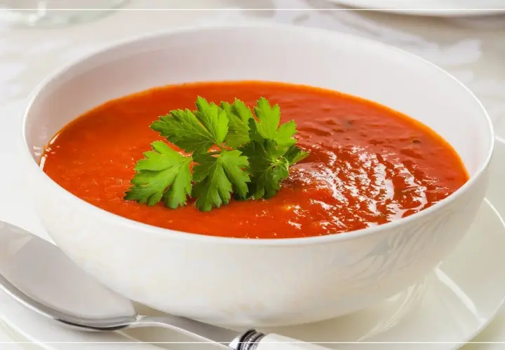 Eine Schüssel cremiger Tomatensuppe mit Petersilie garniert, daneben ein Löffel.