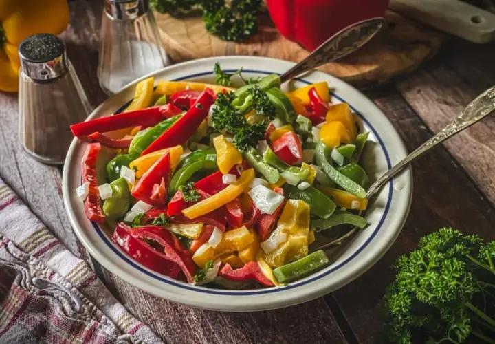 Bunter Salat mit Paprika, Zwiebeln und Petersilie, serviert auf einem rustikalen Holztisch.