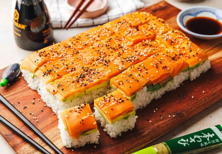 Low-Carb-Sushi mit Lachs und Avocado, bestreut mit Sesam, auf einem Holzbrett.