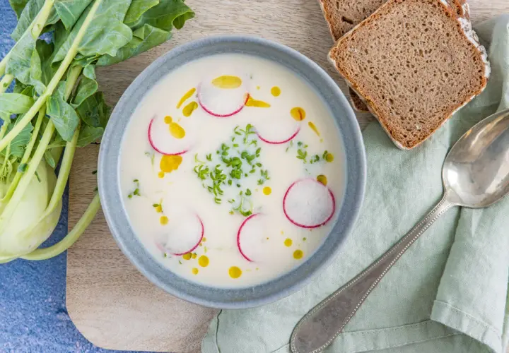 Cremige Kohlrabisuppe low carb, garniert mit Radieschenscheiben und Kresse. Dazu Vollkornbrot und ein Löffel.