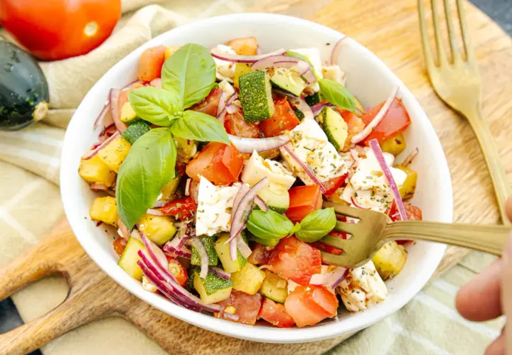 Frischer zucchini-salat mit feta, Tomaten, roten Zwiebeln und Basilikum, garniert mit Kräutern.