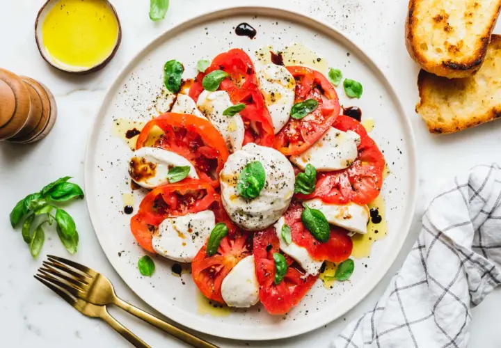 Caprese-Salat mit frischen Tomaten, veganem Mozzarella und Basilikum, beträufelt mit Olivenöl und Balsamico. Dazu geröstetes Brot.