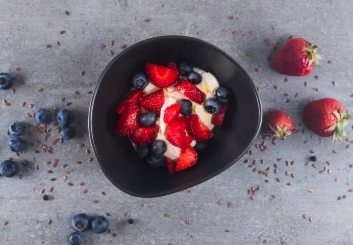 Schüssel mit cremigem low carb Joghurt, garniert mit frischen Erdbeeren und Blaubeeren. Leinsamen verstreut.