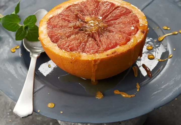 Halber Grapefruit mit Honig beträufelt, serviert auf einem Teller mit Minze. Ein köstliches, grapefruit low carb Frühstück.
