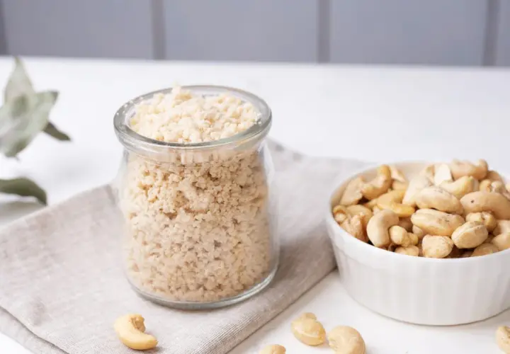 Zutaten für veganen Parmesan selber machen: Cashewkerne in einer Schüssel und fertig gemahlene Masse in einem Glas.