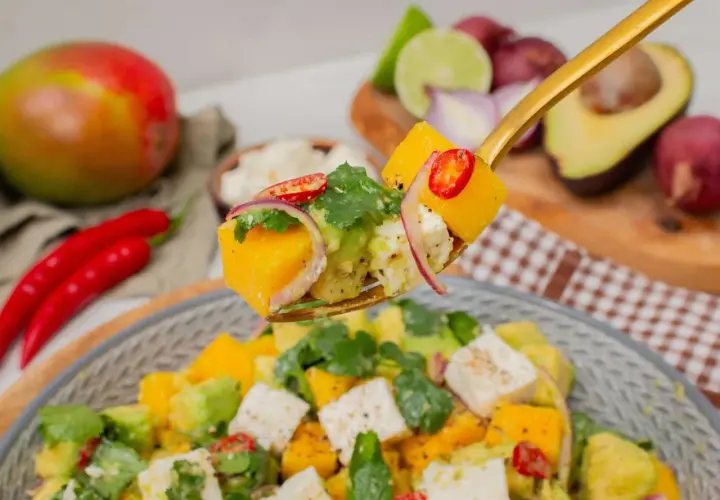 Ein Löffel voller Mango-Salat mit Avocado, Feta, roten Zwiebeln und Chili.