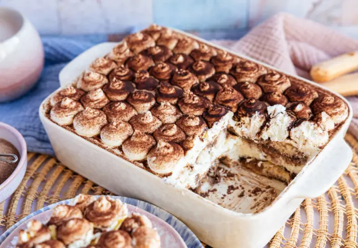 Cremiges, veganes Tiramisu ohne Alkohol, bestäubt mit Kakao. Ein Stück wurde bereits entnommen, was die Schichten aus Creme und Löffelbiskuits zeigt.