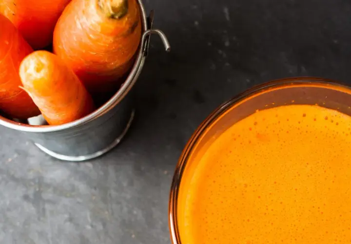 Frische Karotten in einem Eimer neben einem Glas leuchtend orangem Karottensaft. Die Wirkung von Karottensaft ist bekannt für seine Vitamine.
