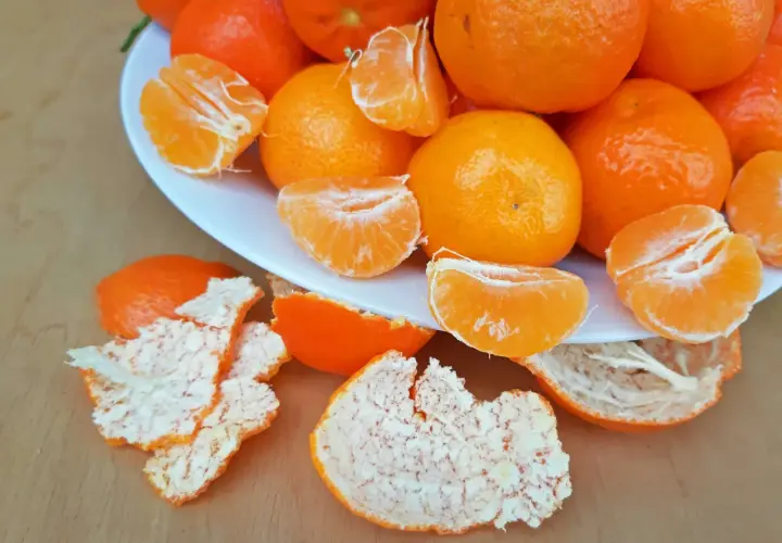 Ein Teller voller saftiger Mandarinen, einige geschält und in Spalten geteilt, daneben die orangen Schalen. Perfekt zum Lagern und Genießen.