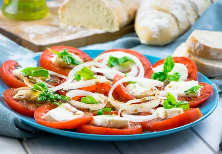 Tomaten-Mozzarella-Salat mit Zwiebelringen und Basilikum, beträufelt mit einem leckeren Dressing. Dazu frisches Brot.