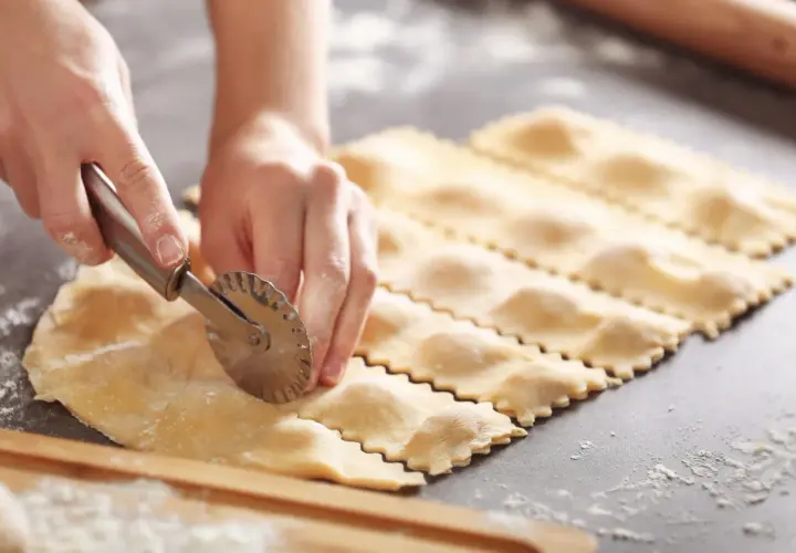 Hände schneiden mit einem Teigrädchen frisch gemachte Ravioli. So lassen sich selbstgemachte Ravioli aufbewahren.