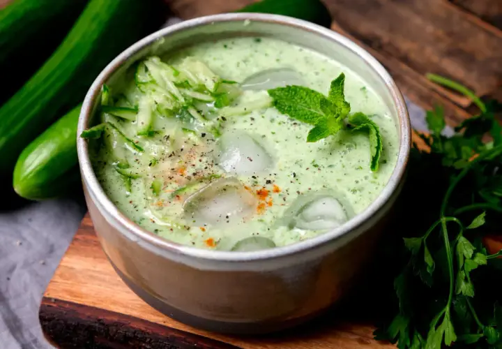 Erfrischende cremige kalte Gurkensuppe mit Eiswürfeln, Minze und geriebenen Gurken, garniert mit Pfeffer und Paprikapulver.