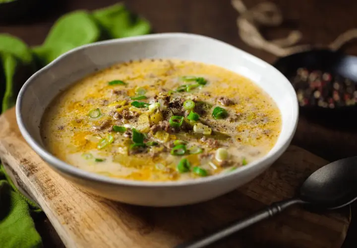 Eine cremige low carb Lauchsuppe mit Hackfleisch und Frühlingszwiebeln, serviert in einer Schüssel auf einem Holzbrett.