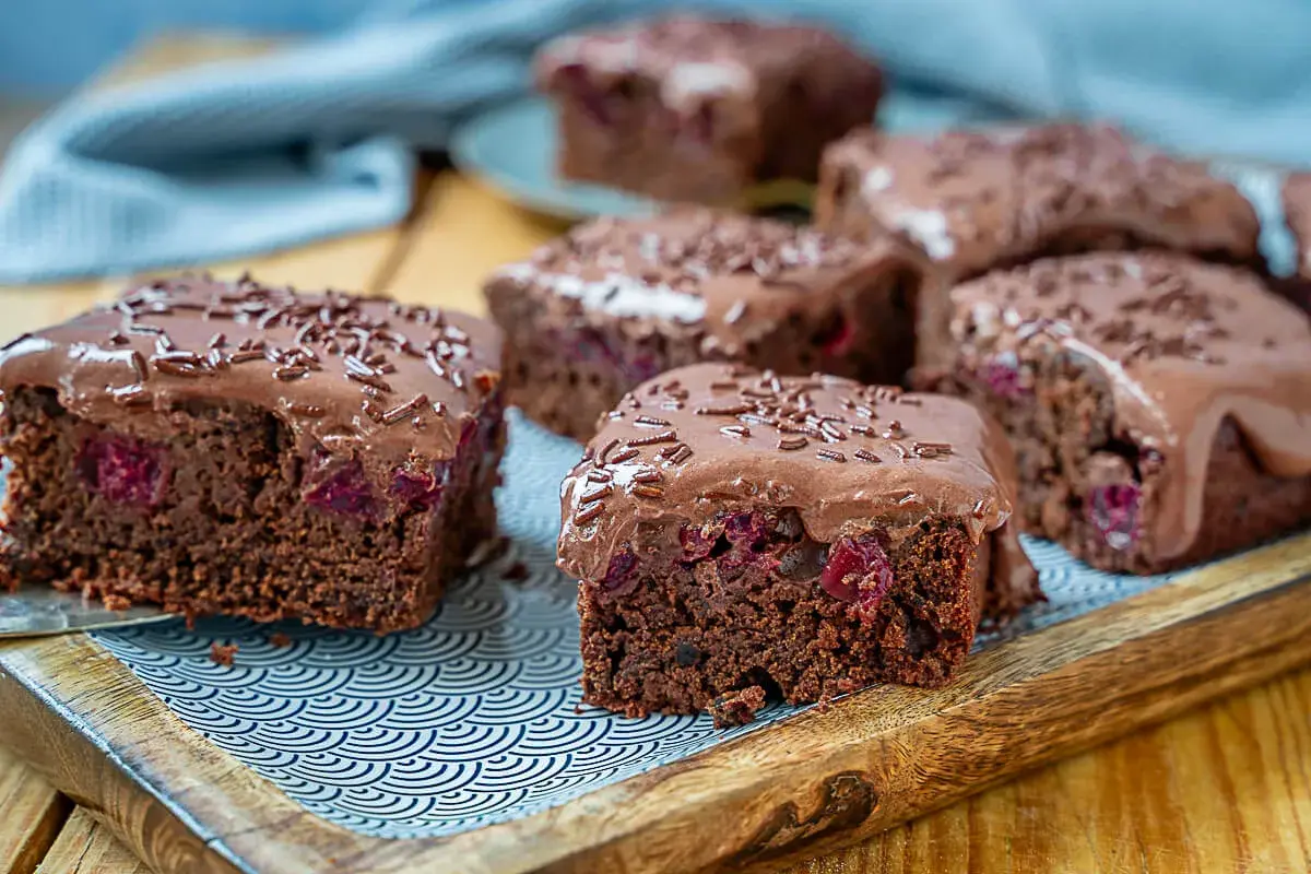Saftiger veganer Blechkuchen mit Kirschen und Schokoglasur, bestreut mit Schokostreuseln. Ein Genuss für alle!