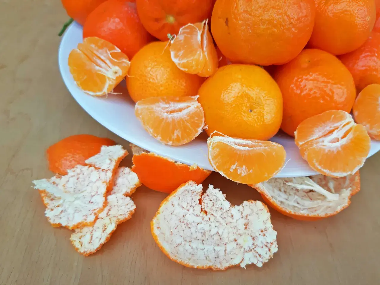 Ein Teller voller saftiger Mandarinen, einige geschält und in Spalten geteilt, daneben die orangen Schalen. Perfekt zum Lagern und Genießen.