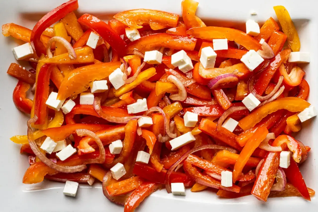Bunter Paprika Salat mit Feta-Würfeln und roten Zwiebeln auf einem weißen Teller.