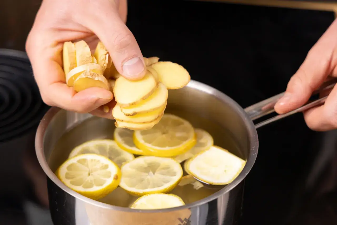 Frische Ingwerscheiben werden in einen Topf mit heißem Wasser und Zitronenscheiben gegeben, um einen wohltuenden Ingwer-Zitronen-Tee zuzubereiten.